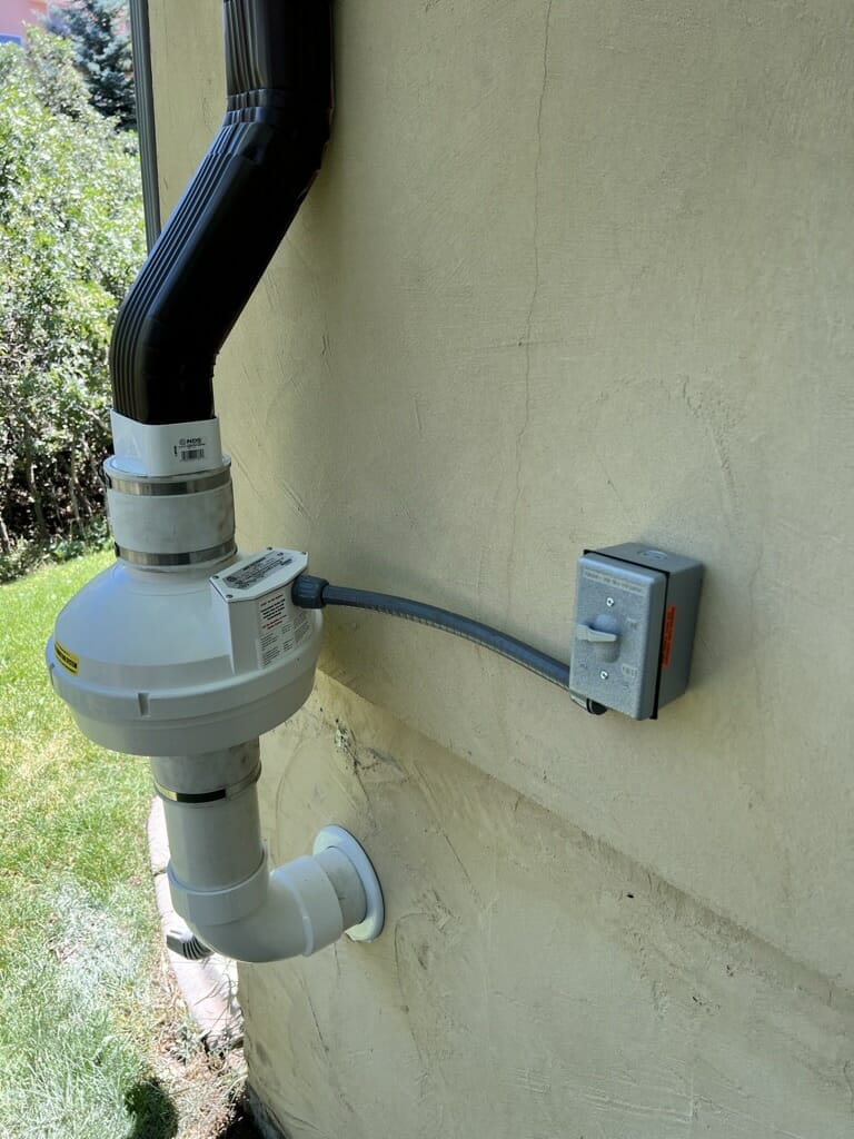Close-up of the radon mitigation system fan unit mounted outside a home